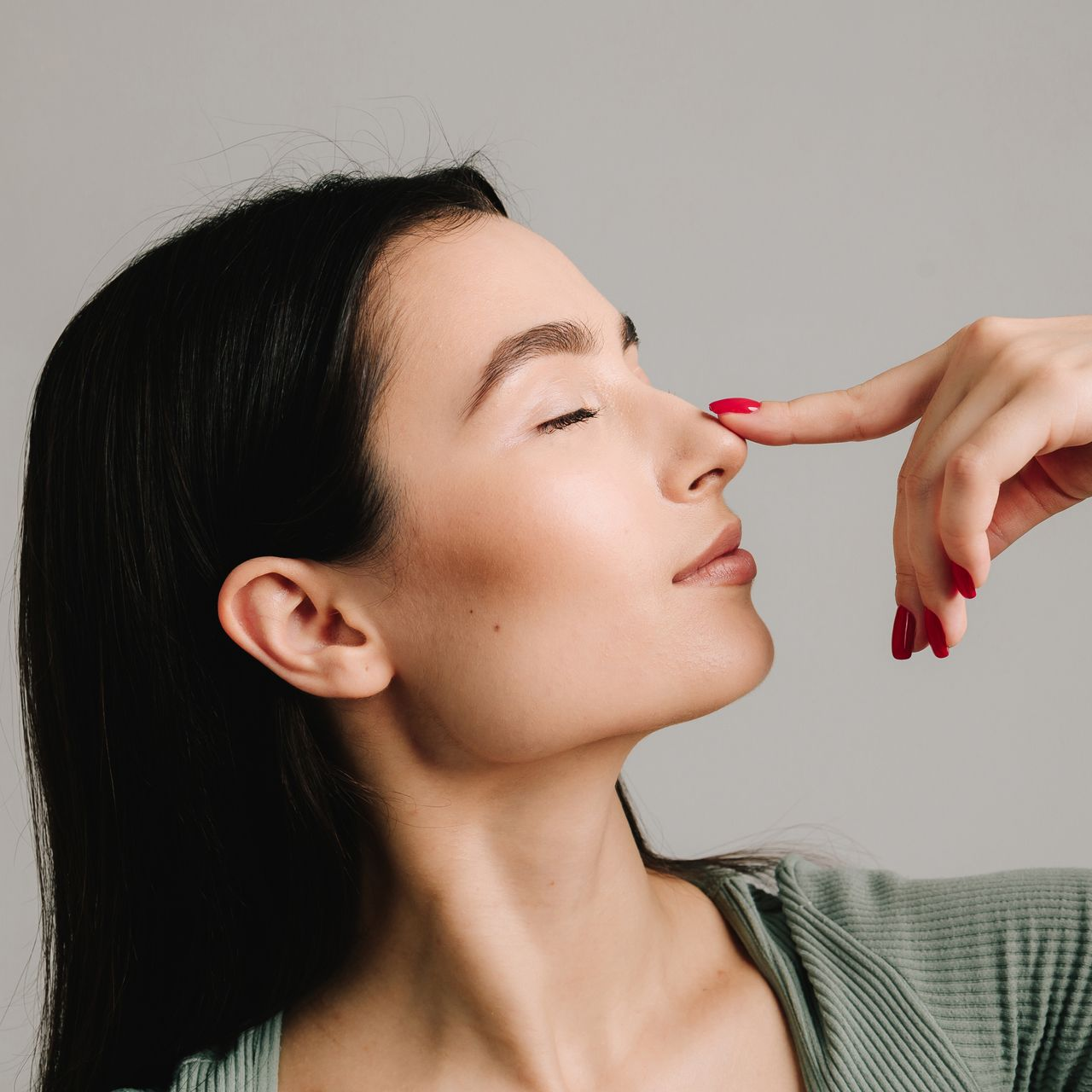 Close-up of a person pinching their nose, eyes closed, against a light background