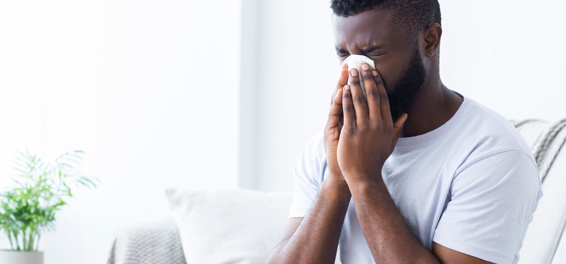 Person sitting on a couch, holding tissues to their face, looking unwell