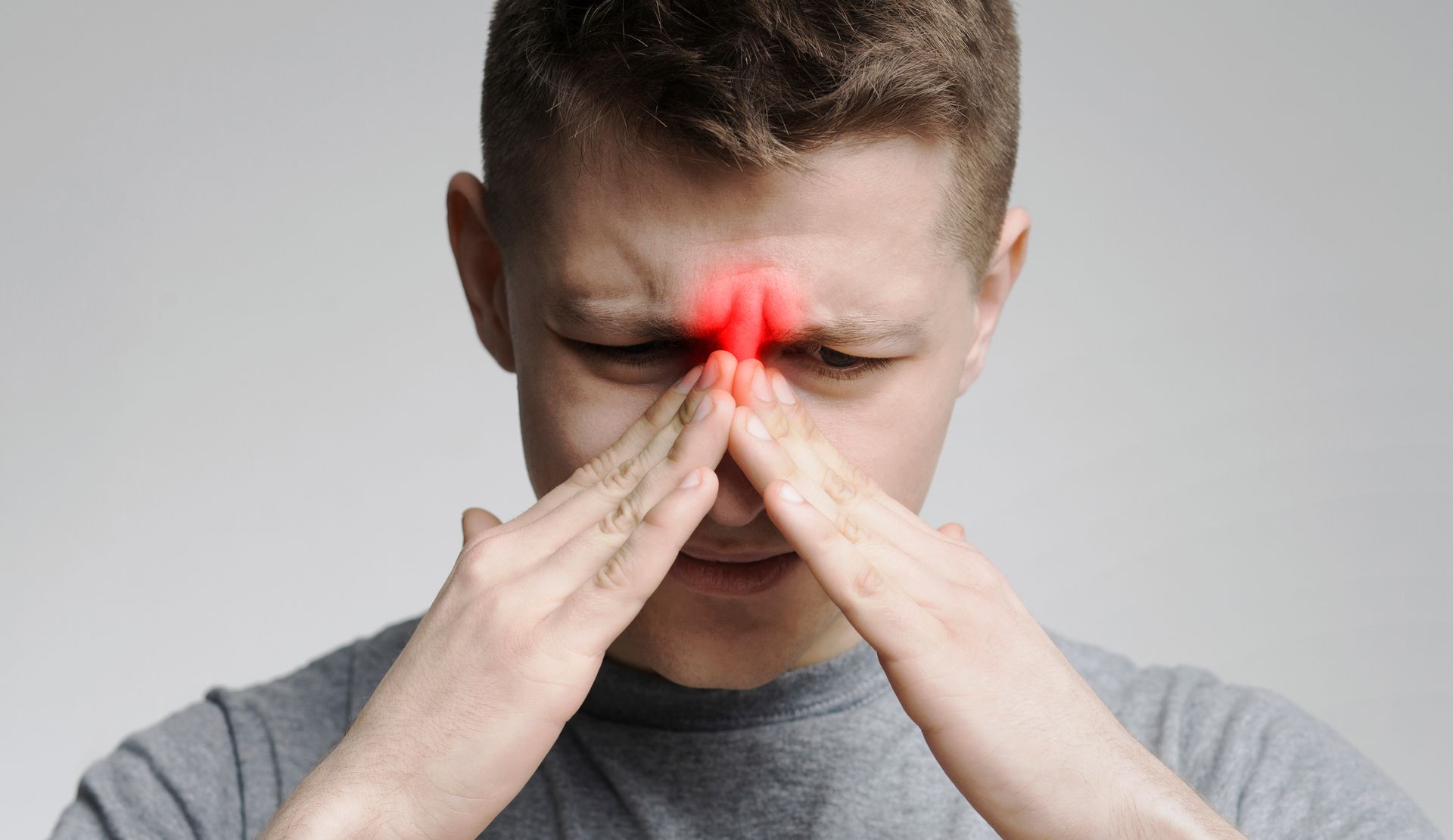 Person pressing fingers to nose with red highlight over the bridge, suggesting sinus pain or headache
