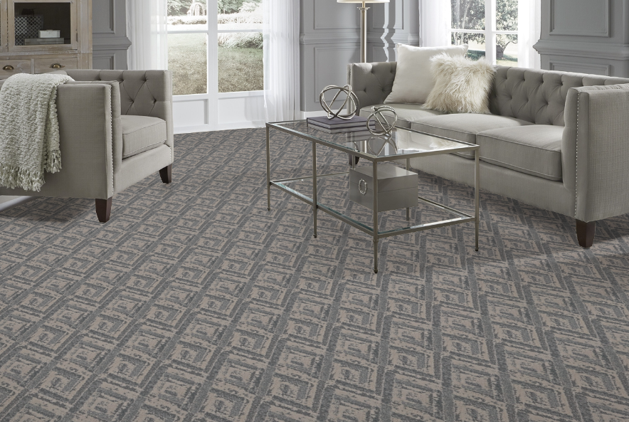 Living room with gray patterned carpet, gray sofa, armchair, and glass coffee table.