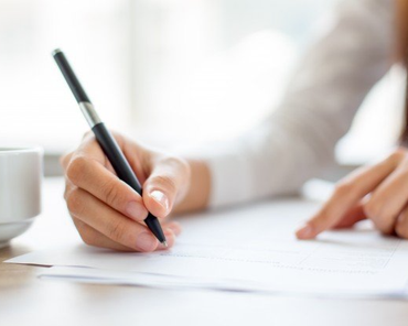 Hand writing on paper with a black pen at a table, with another hand nearby