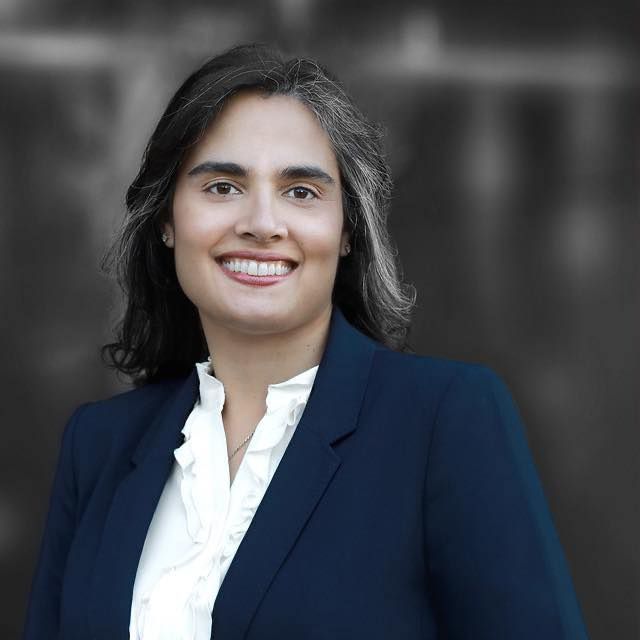 Woman with brown hair smiling in a blue blazer and white ruffled shirt.