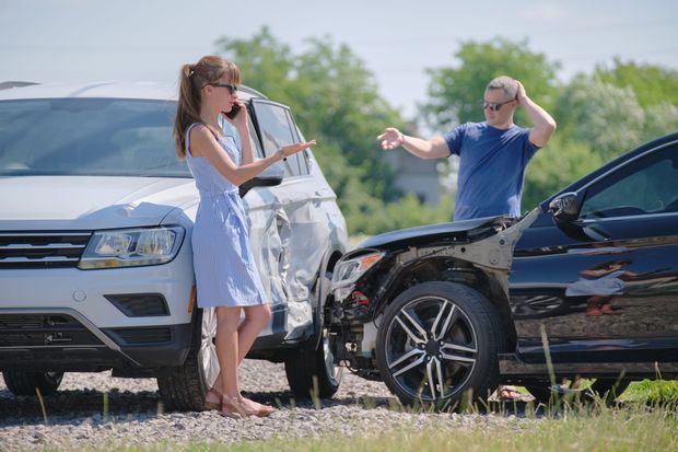 Two cars with front-end damage on a roadside, with two people standing nearby and talking.