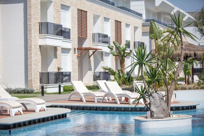Resort pool with white lounge chairs and palm trees beside a modern apartment building