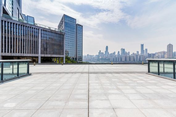 Rooftop terrace overlooking a city skyline beside a modern glass building under a cloudy sky
