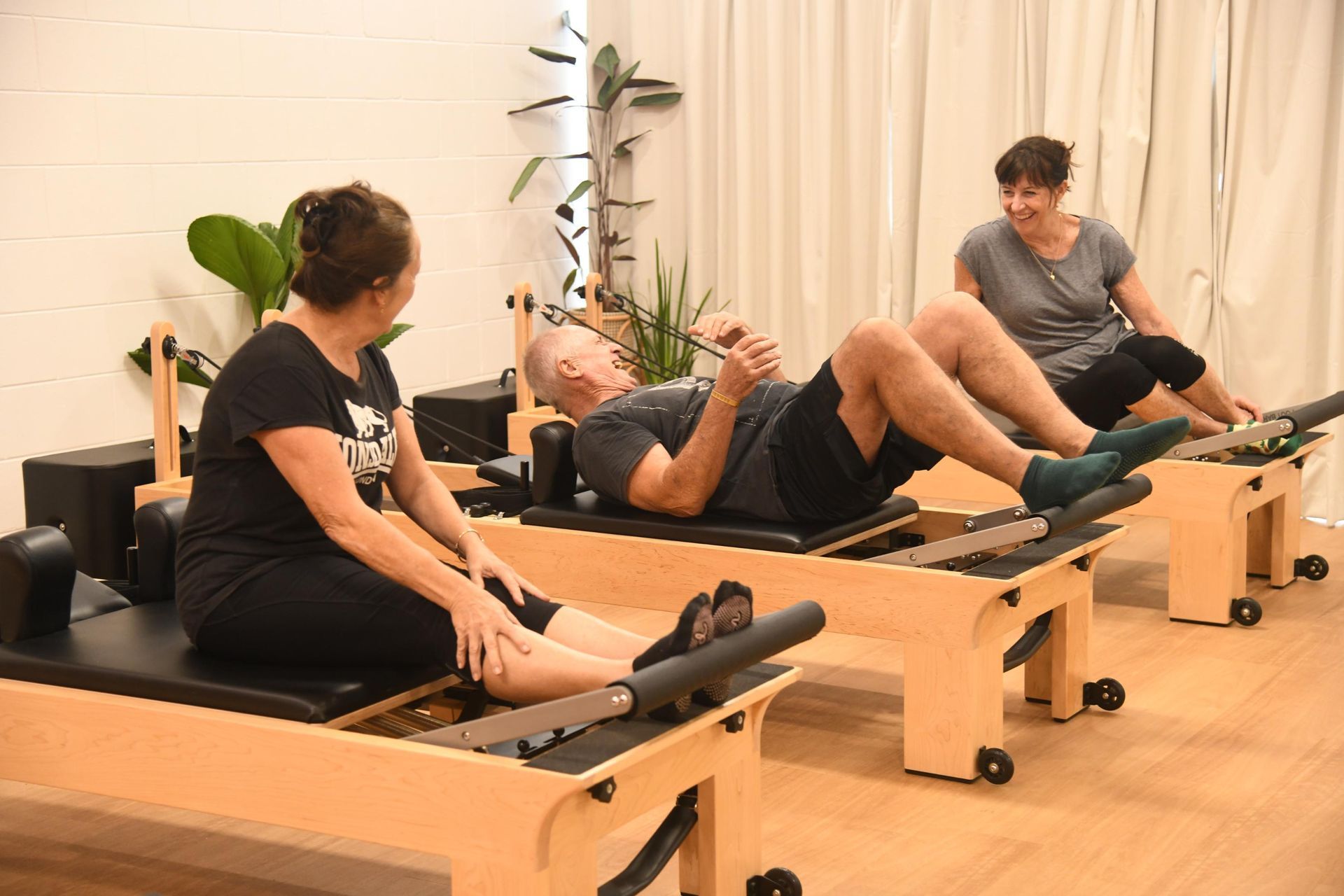 People exercise on wooden Pilates reformers in a bright, indoor studio.