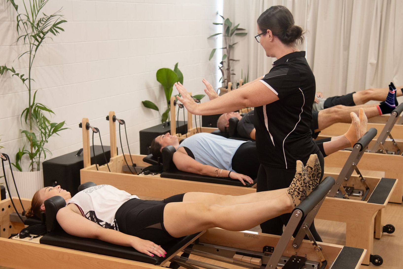 Pilates class with instructor guiding students on reformers in a bright studio.