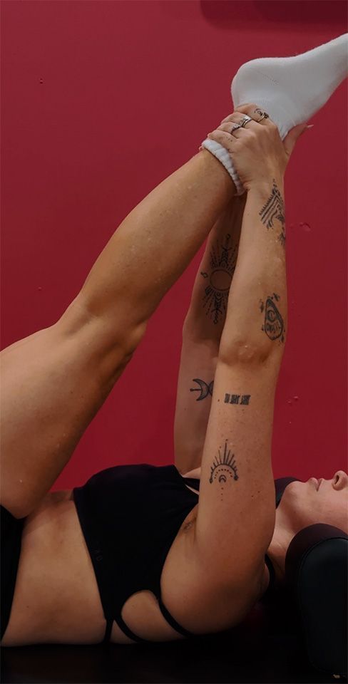 People exercise on wooden Pilates reformers in a bright, indoor studio.