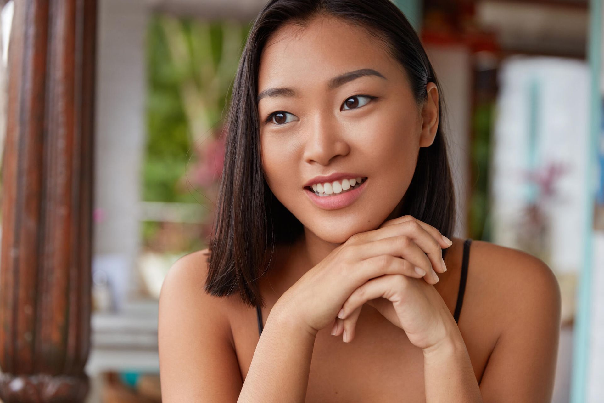 Smiling woman resting her chin on clasped hands in a softly lit indoor setting
