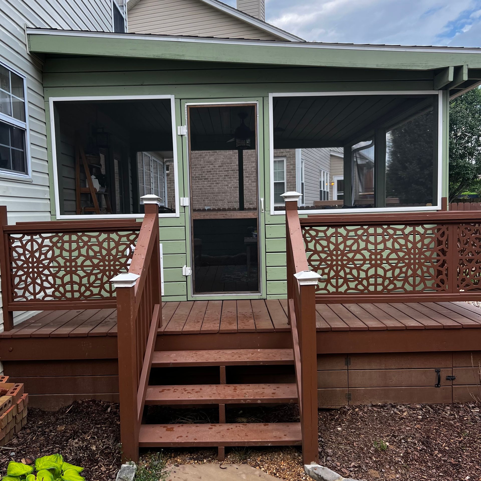 Wooden deck with steps, table, chairs, potted plants, and brick house.