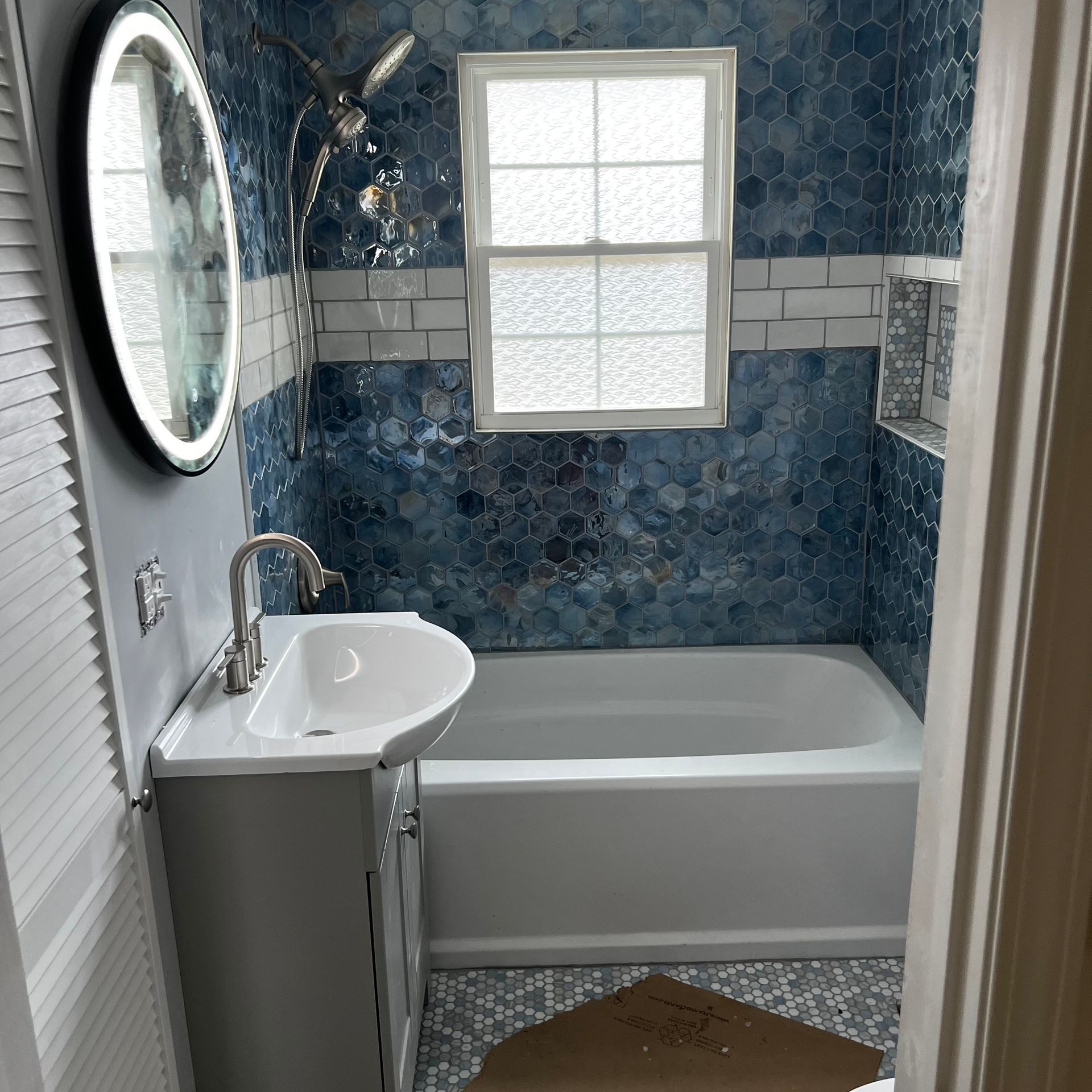 Modern white bathroom with black accents, including a lit mirror, sliding glass shower, and vanity with a white countertop.