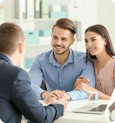Couple smiling at financial advisor in office. They are seated at a table with a laptop and glass of water.