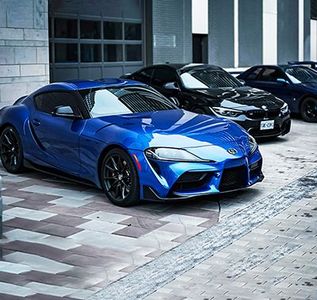 Blue sports car parked in front of garage, with three other cars lined up in background.