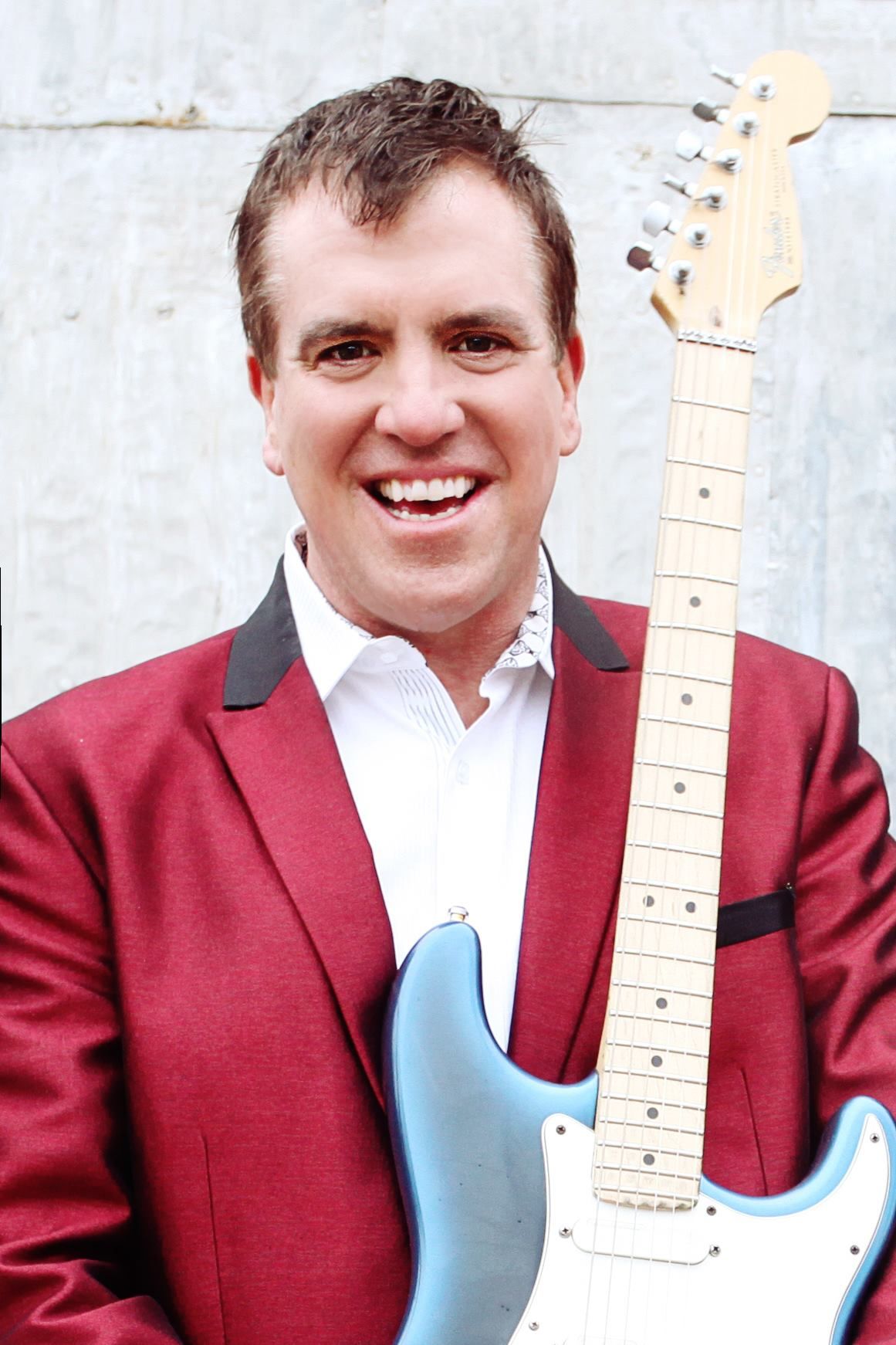 A man in a red jacket is holding a blue guitar