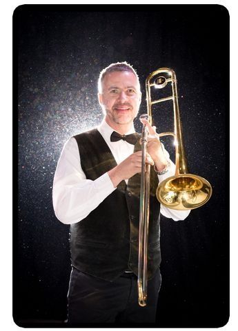 A man in a tuxedo is holding a trombone.