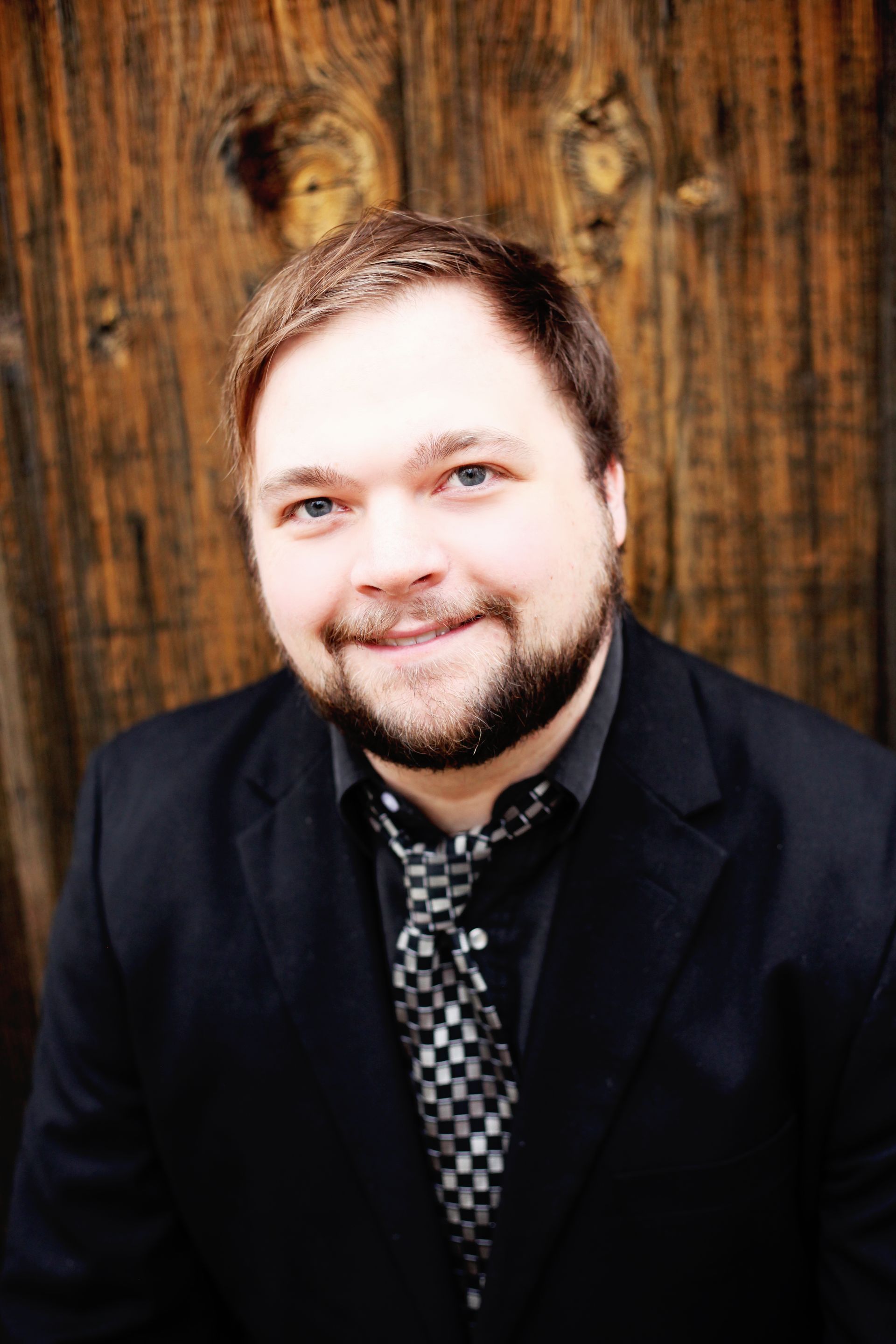 A man in a suit and tie is smiling in front of a wooden wall.