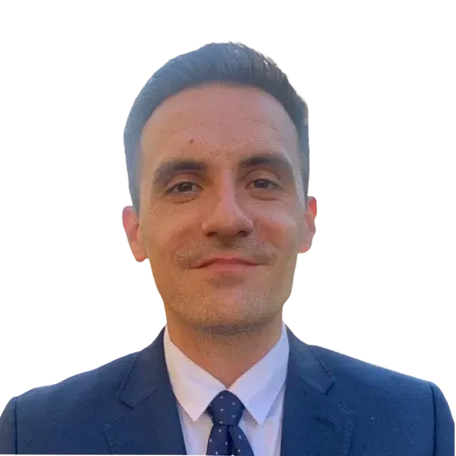 Man in a dark blue suit, white shirt, and patterned tie, smiling.