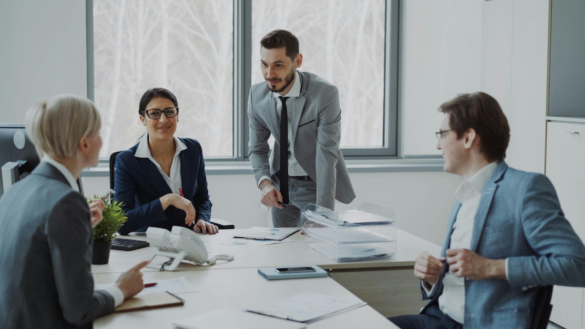 Business meeting in a bright office, with four people discussing documents around a conference table.