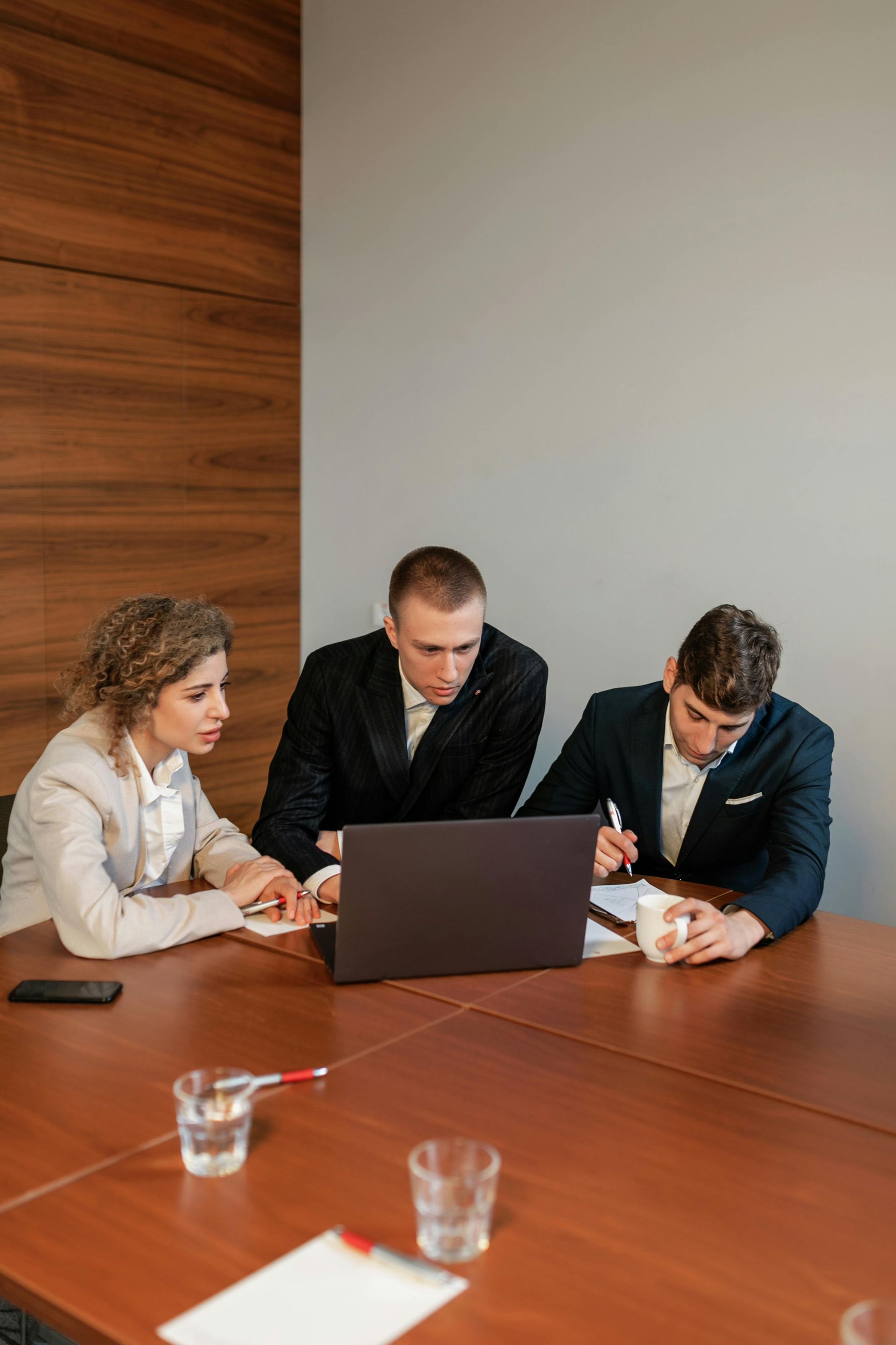 Three people meeting around a laptop at a conference table in a modern office