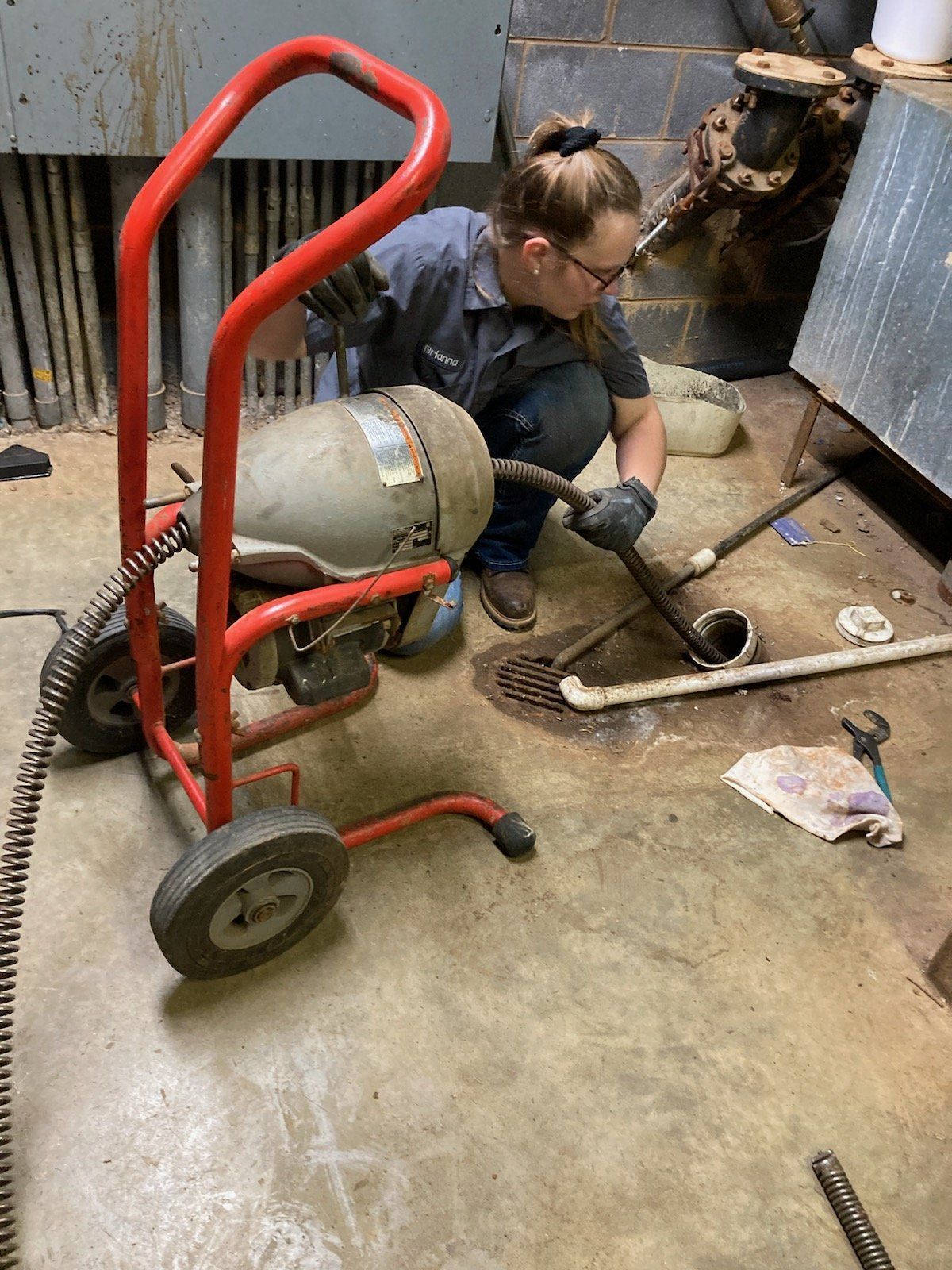 A woman is kneeling on the floor using a drain cleaner.