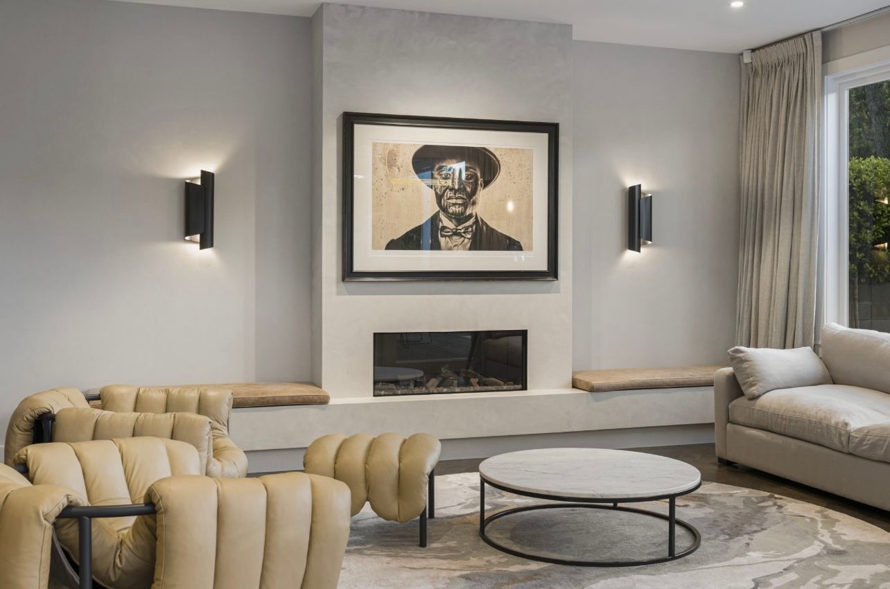 Modern living room with beige sofas, round coffee table, fireplace, and framed artwork above the mantel
