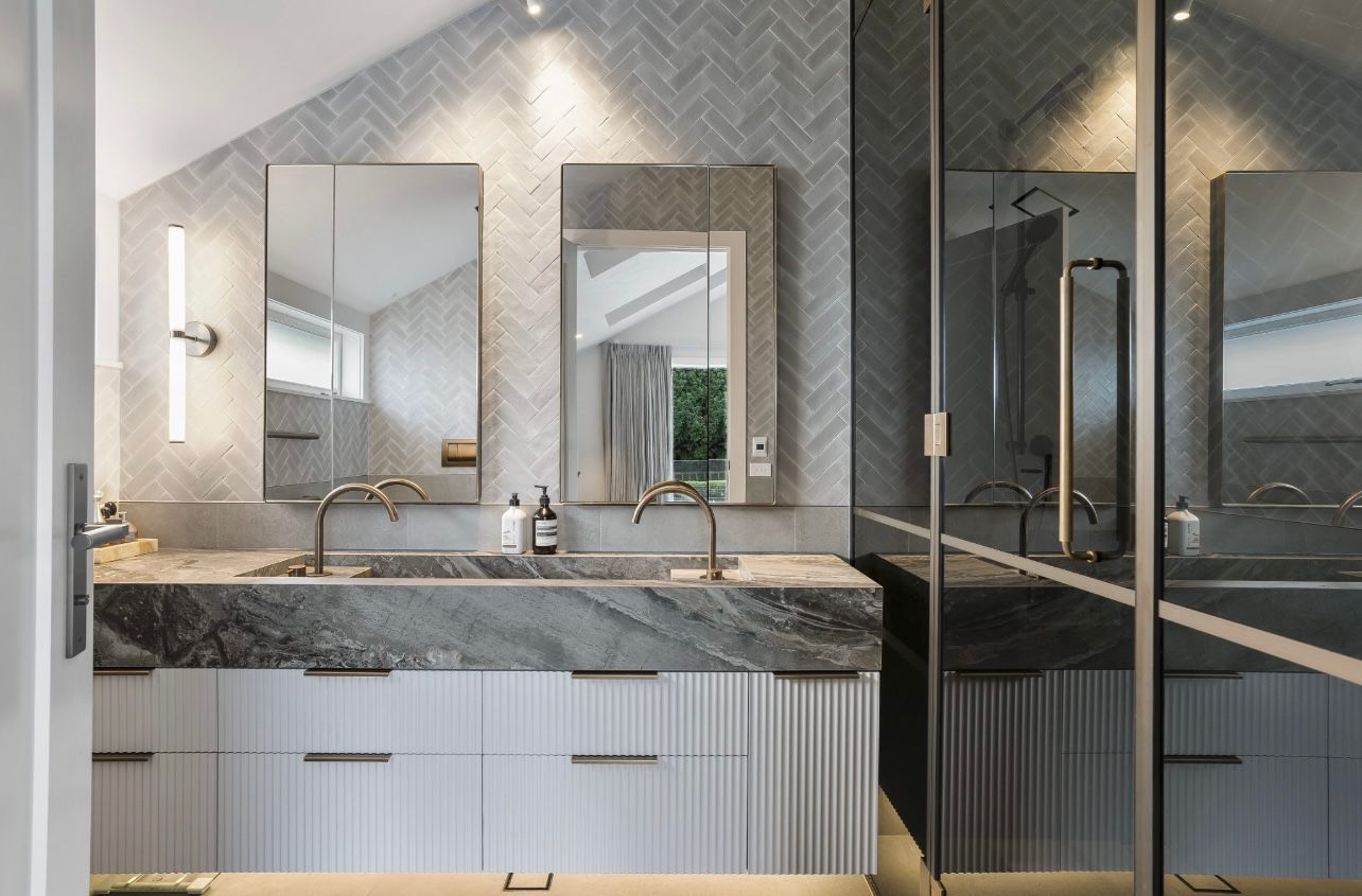 Modern bathroom with double vanity, large mirrors, marble counters, and a glass shower enclosure