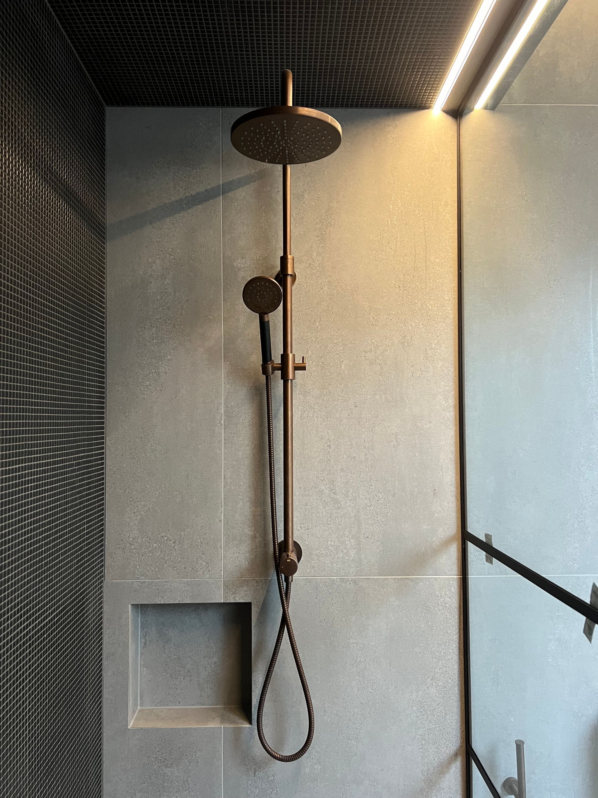 Modern shower stall with a ceiling-mounted showerhead and handheld sprayer on a tiled wall.