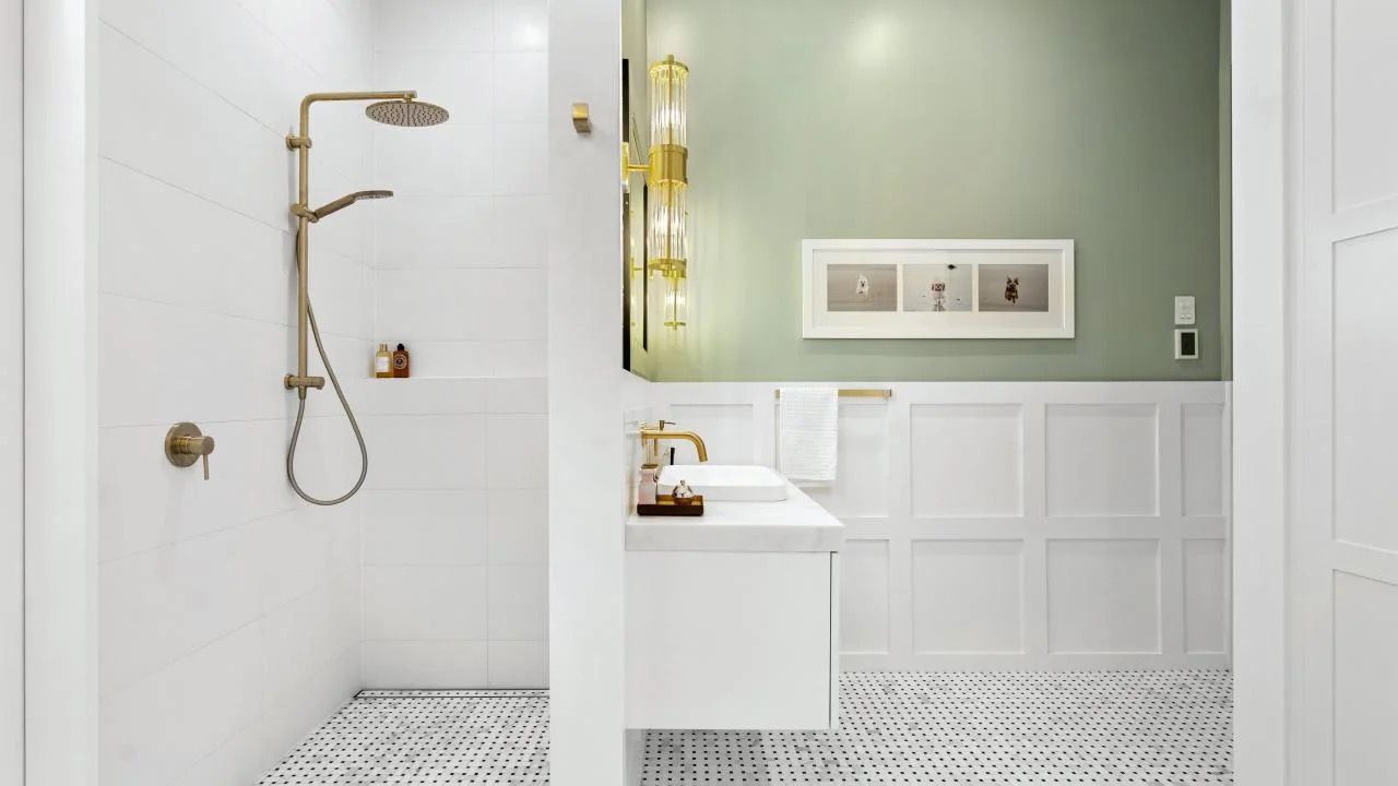 Luxury bathroom with white marble shower, gold fixtures, pedestal sink, and large mirror