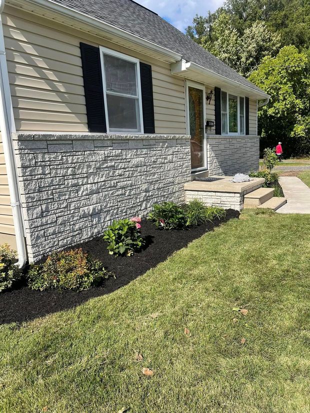 A house with a stone facade and black shutters is sitting on top of a lush green lawn.