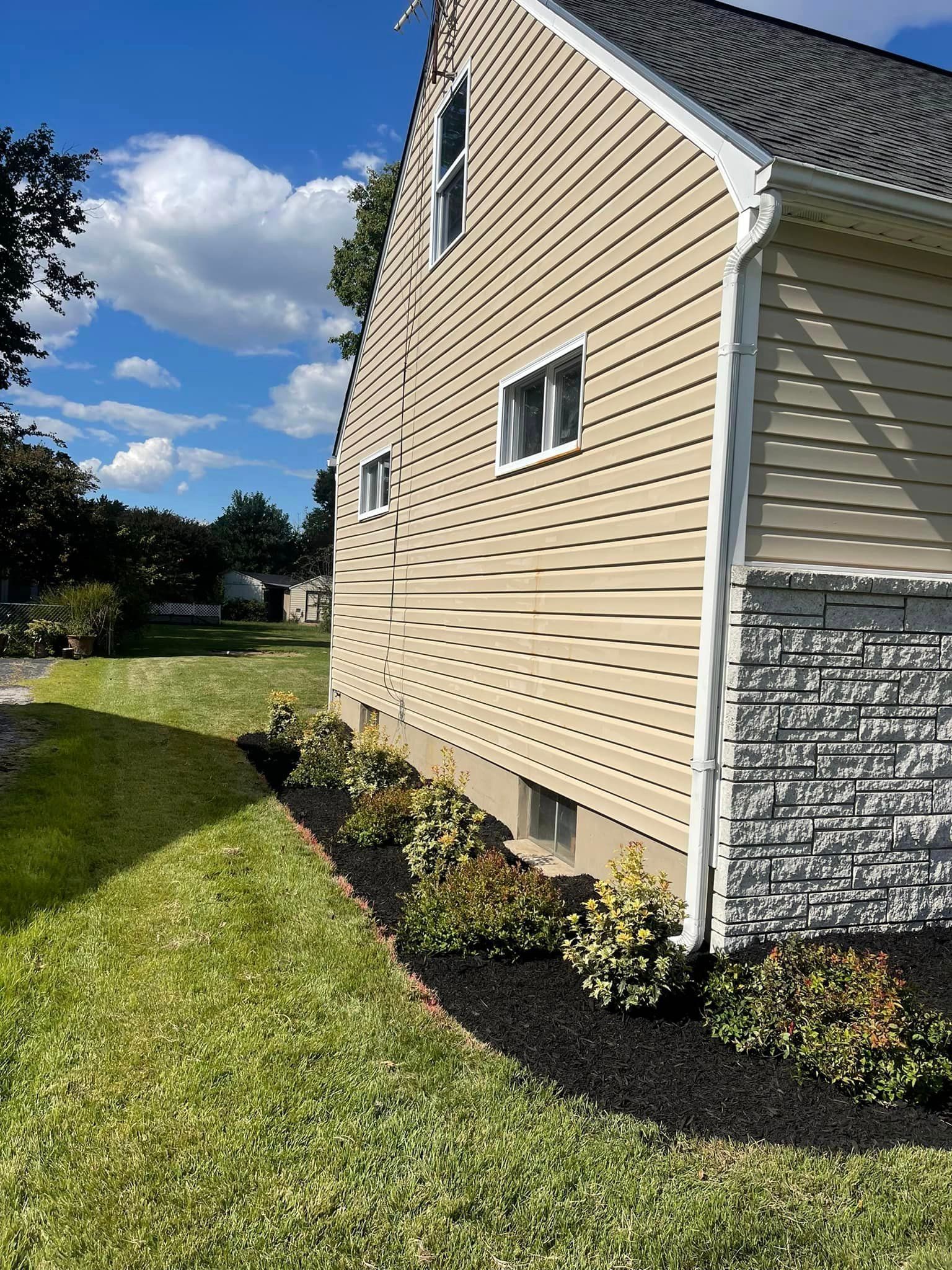 The side of a house with a lot of plants in front of it.
