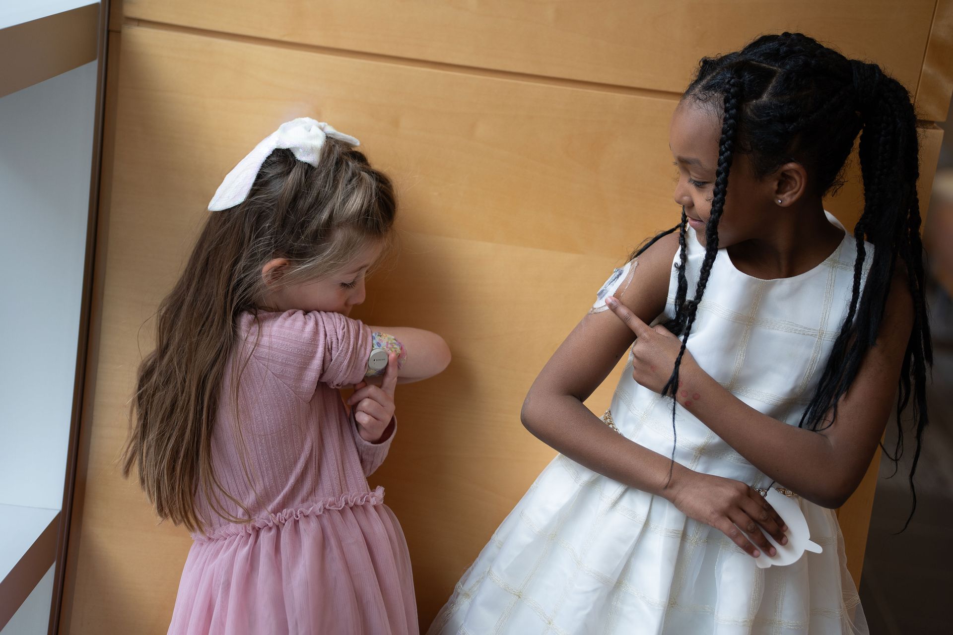 Two little girls showing each other their CGM devices.