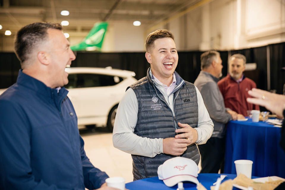 Two male event participants laughing together in the airplane hangar prior to departure to Vegas.