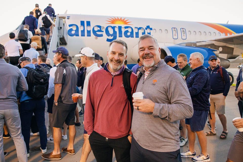 Two event participants standing outside Allegiant airplane on tarmac as guests board for Vegas.