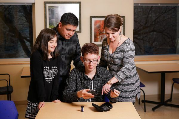 A family standing around a table looking at a a blood glucose monitor for their son/brother