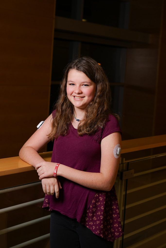 A young girl with a needle in her arm is standing next to a railing.