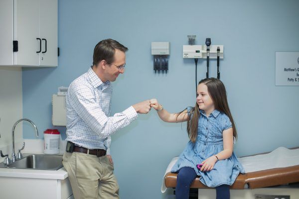 Male doctor fist-bumping with young T1D female patient in BDC exam room.