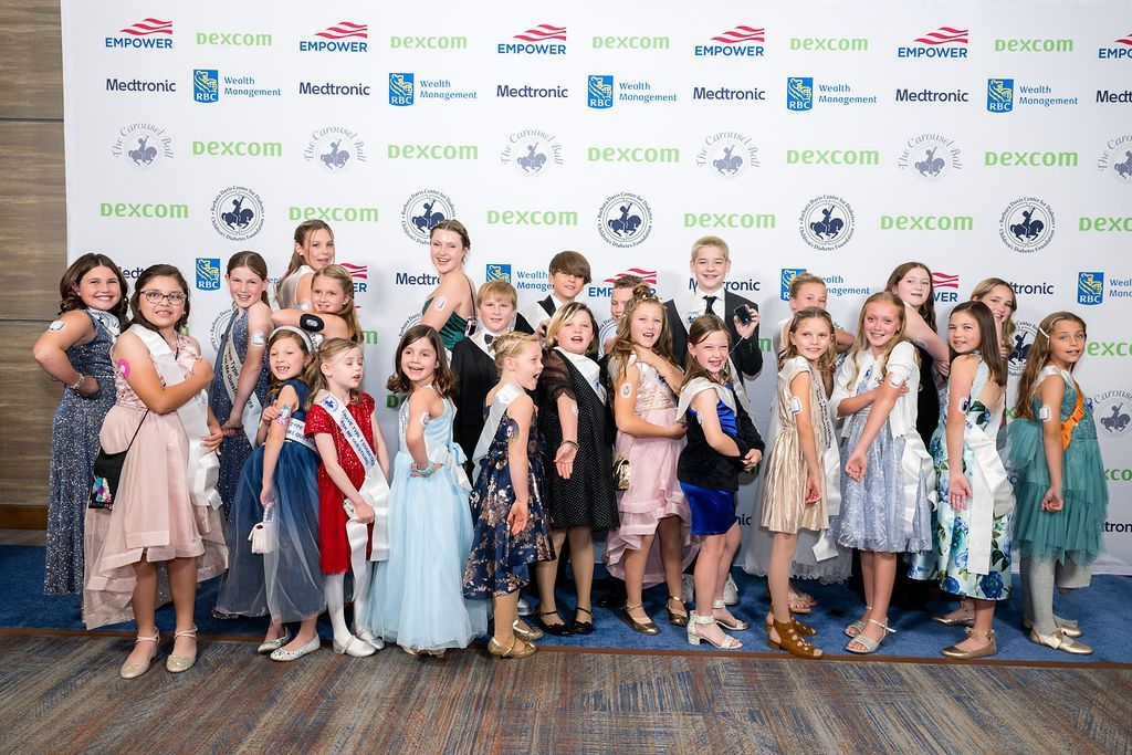 Large group of T1D advocates posing in their sashes on the blue carpet at Carousel Ball.
