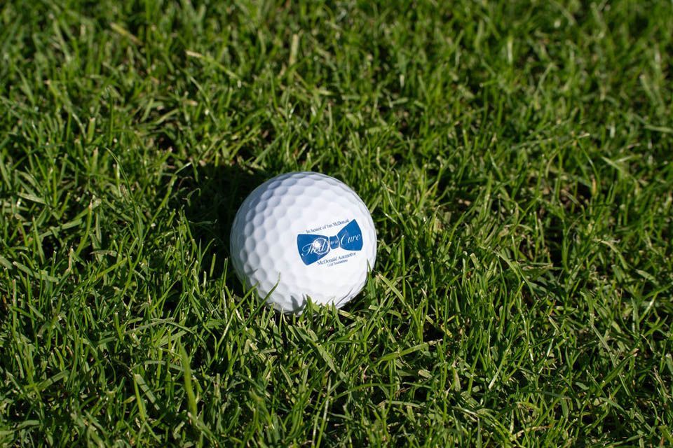 Closeup of commemorative Tied to a Cure golf ball lying in the grass.