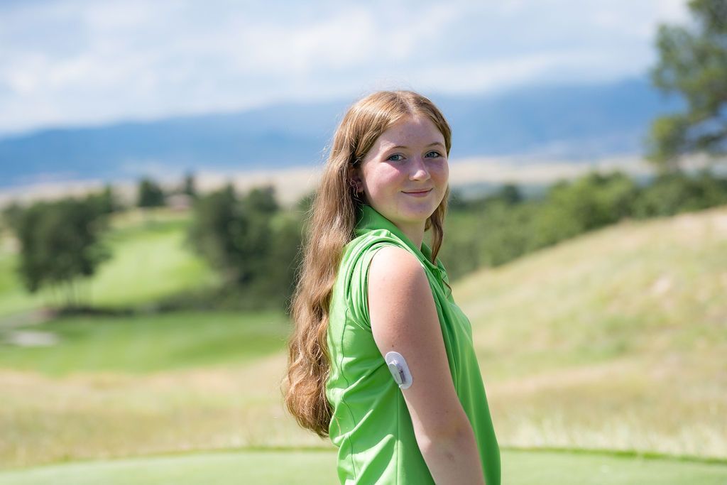 Girl standing on the golf course, showing her CGM device on the back of her arm.