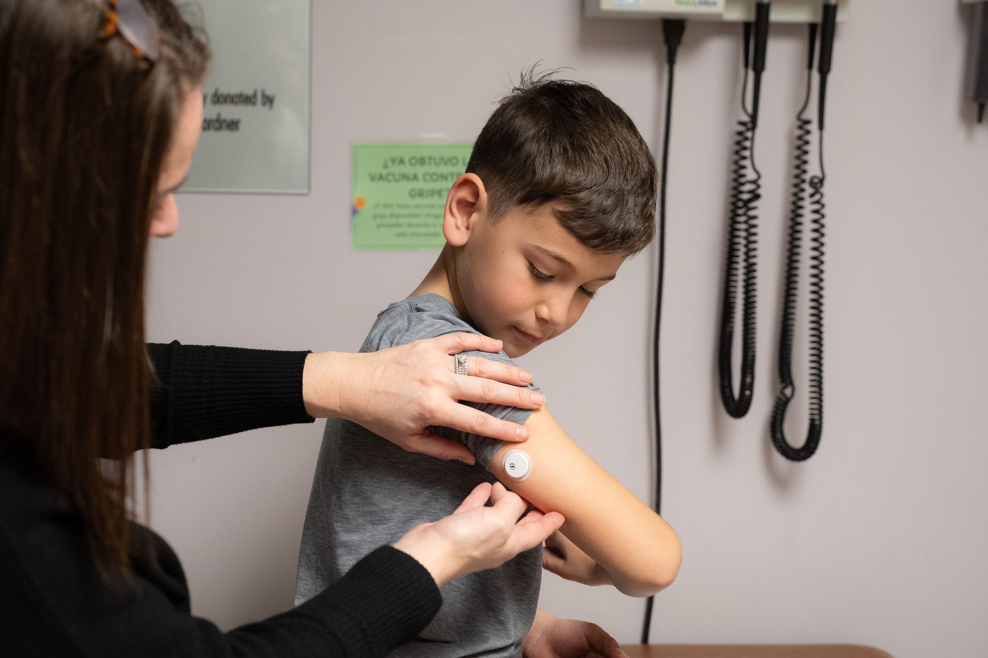 Young boy getting his CGM device applied to his arm by medical staff.