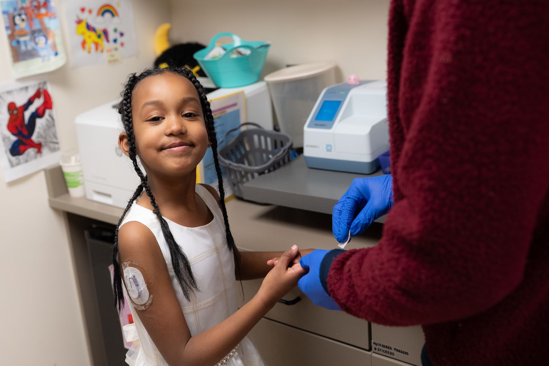 Young girl with a CGM on her arm, getting her finger pricked to test her blood sugar levels.