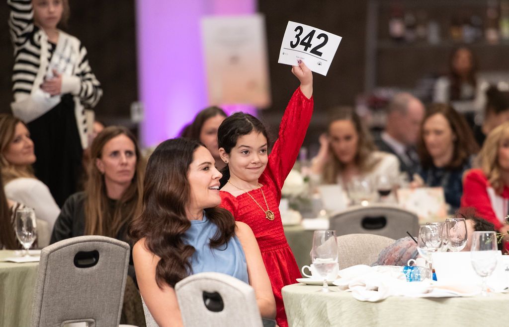 Young girl holding up her paddle to donate money during the paddle raise.