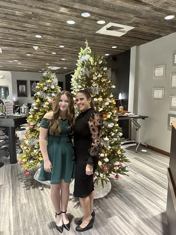Two women posing in front of decorated Christmas trees. 