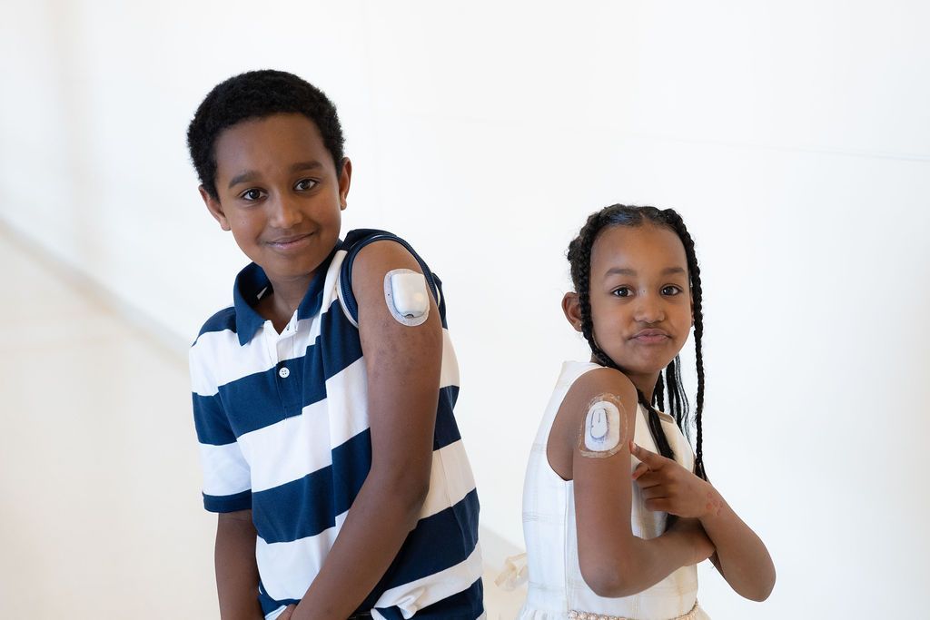 Two young girls smiling while showing each other their insulin pumps.