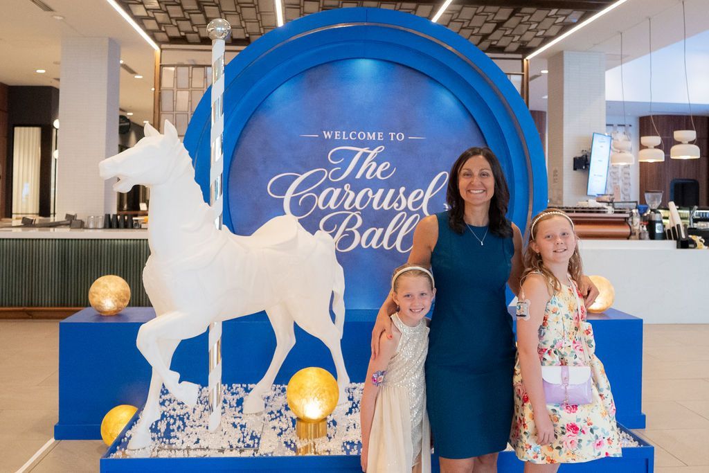 Carousel Ball horse and sign with two advocates and their mom in front of it
