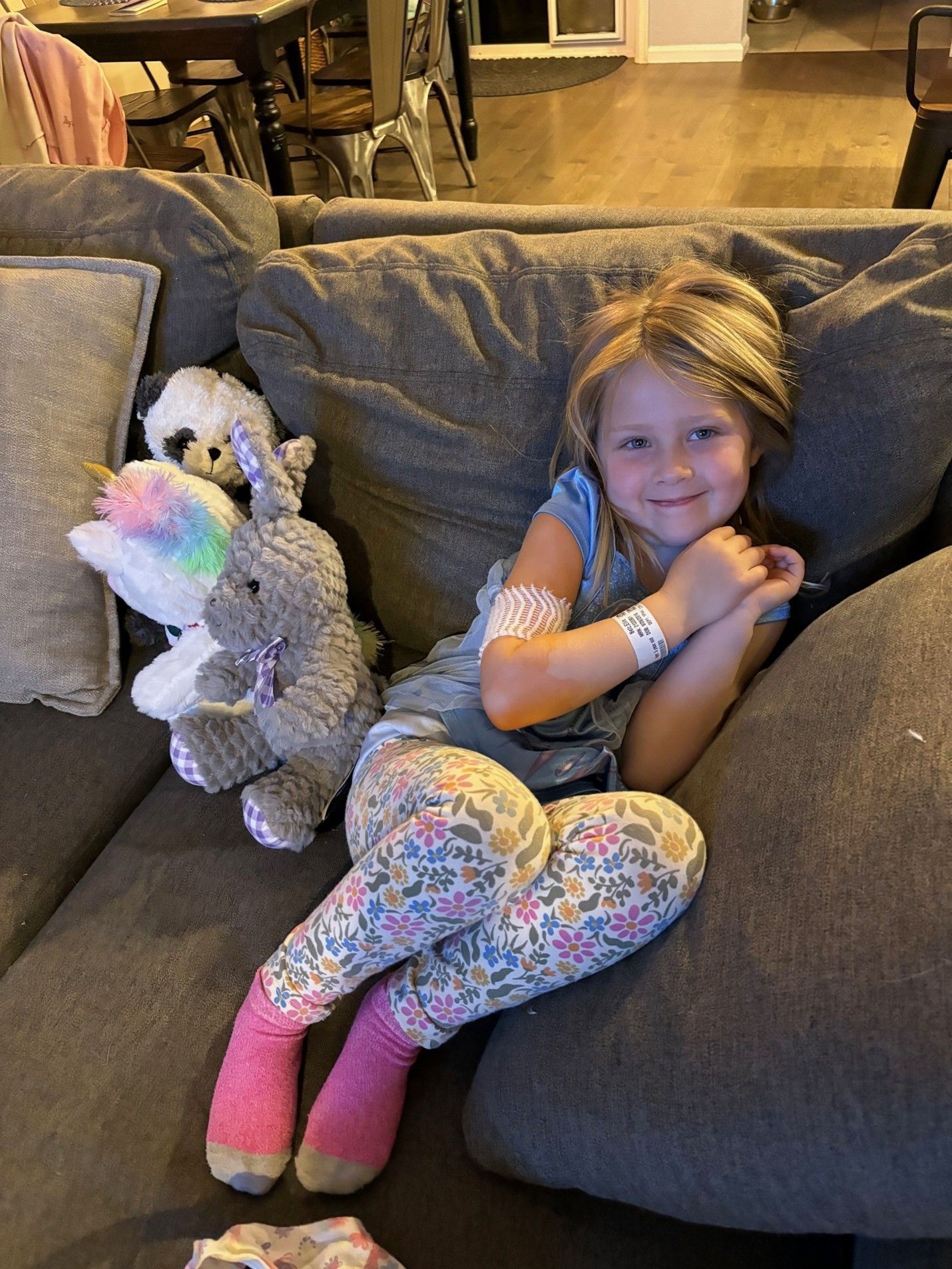 Smiling young girl on couch with bandage on arm and hospital bracelet on wrist