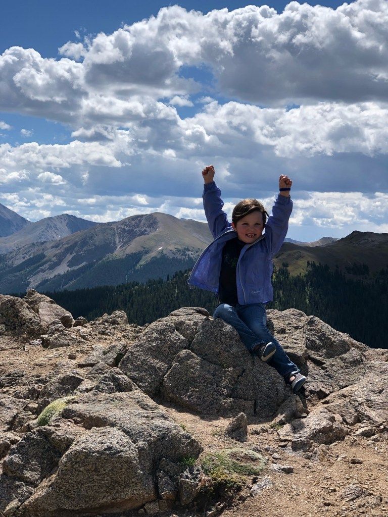 Frankie is sitting on a Colorado mountain rock with her arms in the air.