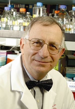 A man in a lab coat and bow tie is smiling