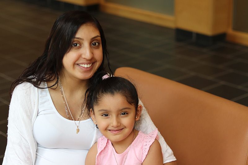 A woman and a little girl are sitting on a couch and smiling for the camera.