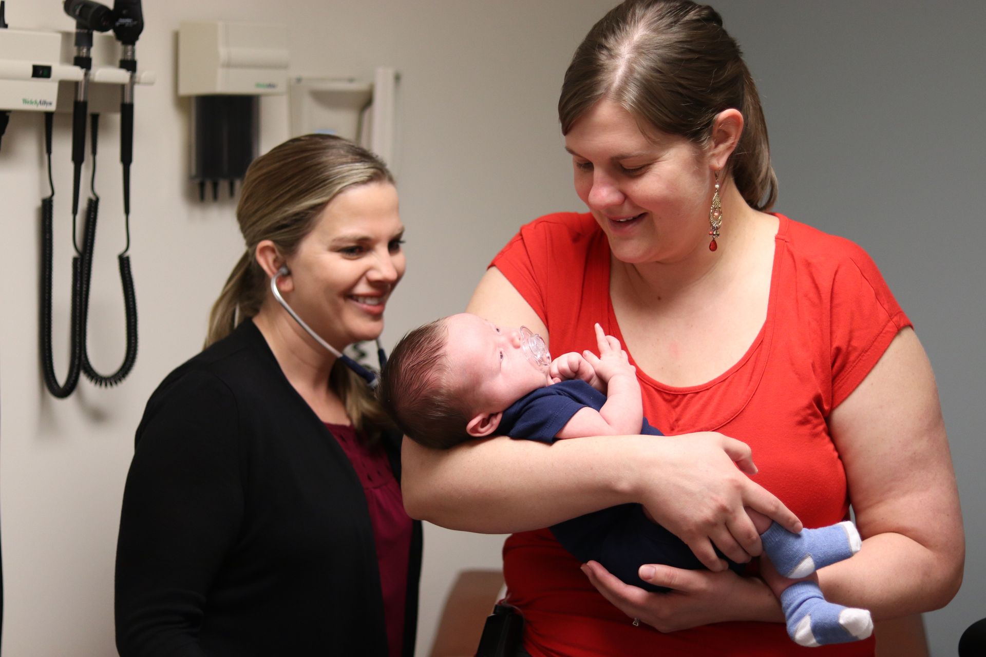 New T1D mother holding her newborn and smiling as doctor examines them both. 
